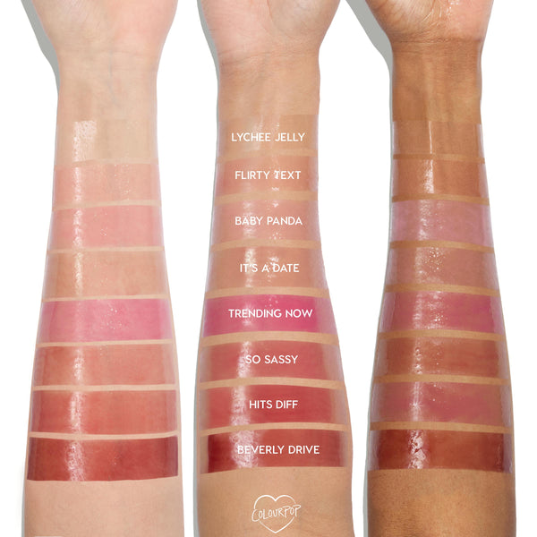 Glossy lip oil swatches, from clear to rose and deep berry, shown on three arms in light, medium, and deep skin tones, labeled Lychee Jelly, Flirty Text, Baby Panda, It’s a Date, Trending Now, So Sassy, Hits Diff, Beverly Drive; ColourPop 100% Juicy So Juicy Lip Oil Set.