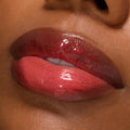 Glossy lips wearing Pack Member Lip Set, a sheer cherry-red tint with fine red shimmer and mirror shine on medium‑deep skin; close-up swatch highlights smooth, plump finish and sparkle for product detail; ColourPop Lip Set.