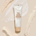 Fourth Ray Beauty The Lightweight hydrator tube showcasing copper lettering, resting over a milky cream swatch on a beige backdrop with pampas grass; ultra-light ColourPop Face Moisturizer in a frosted white tube with a peach cap.