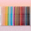 Charmer Crème Gel Liner displayed among the full rainbow lineup of ColourPop Crème Gel Liner twist-up pencils, tips extended from white through brights to black, standing in a row on a pink background with heart, star, and smiley doodles.