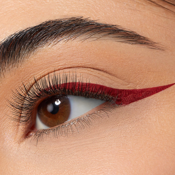 Wine-red winged eyeliner shapes a brown eye, a sharp cat-eye along the upper lash line created with ColourPop BFF Liquid Liner in Try Me; smooth matte lid and long lashes shown in a close-up.