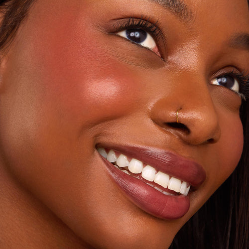Blush n’ Pout ColourPop Cheek & Lip Set adding a warm rosy flush and berry-mauve satin lip to a smiling model in a close-up beauty shot, highlighting smooth skin, defined lashes, and a small gold nose ring under soft studio lighting.