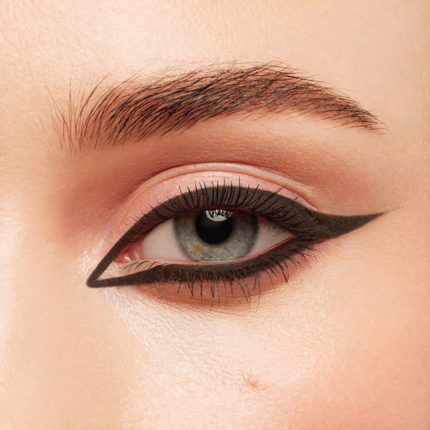 Defined black lashes coated with ColourPop BFF Mascara in Black on Black, fanning a blue‑gray eye framed by bold graphic double‑wing eyeliner; close‑up beauty shot showcasing clump‑free length and volume.