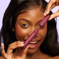ColourPop BFF Mascara in Wine O’Clock, a burgundy volumizing formula, shown as a model opens the star-patterned wand near her lashes; close-up with lime green eyeshadow against a soft lavender background.