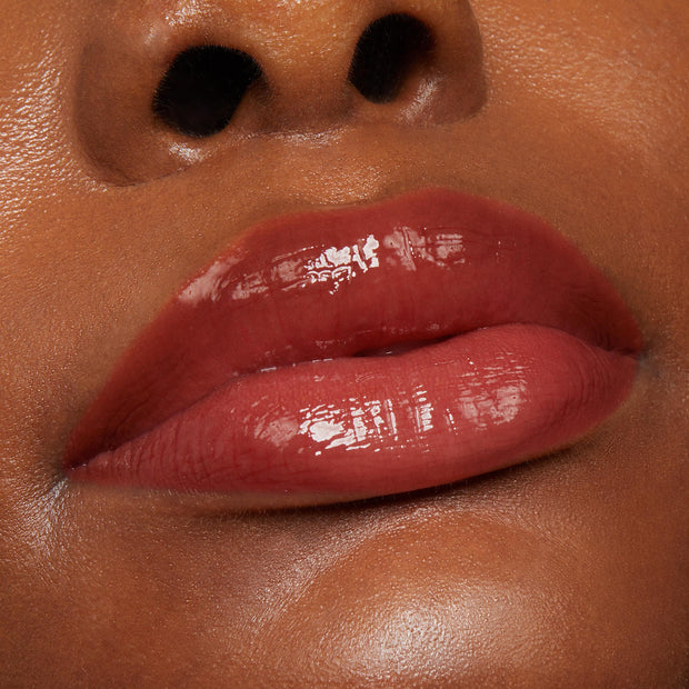 Glossy lips wear Vampy Lips Lux Lip Oil, a ColourPop Lux Lip Oil, in a tight beauty close-up, showing a rich berry-brown tint with high shine, smooth cushioned texture, and a hydrated finish against warm, even skin.