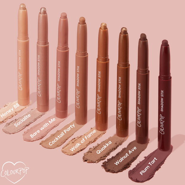 ColourPop Shadow Stix in Walnut Ave stands open with a creamy taupe-brown swatch beneath it, shown among other ColourPop Shadow Stix shades on a blush pink background for easy shade comparison.