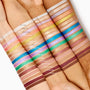 Friday Feels Shadow Stix swatch - one creamy, shimmery stripe - glides across multiple forearms of different skin tones, shown alongside the full ColourPop Shadow Stix lineup to demonstrate pigment payoff and blend in bright studio lighting.