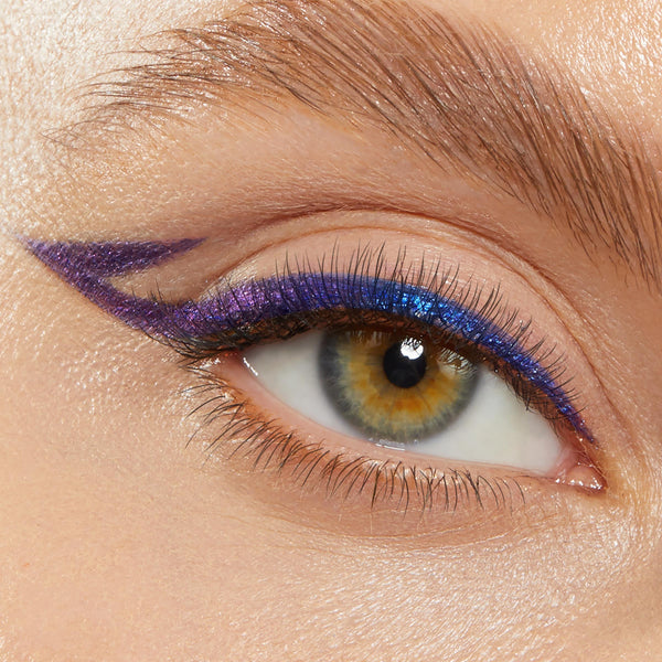 Winged eyeliner defines a close-up eye, wearing ColourPop Crème Gel Liner in Good Shift - a creamy blue-to-purple duochrome that lines the upper lash line with a sharp extended flick and subtle double wing, on a bare lid and groomed brow.