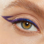 Winged eyeliner defines a close-up eye, wearing ColourPop Crème Gel Liner in Good Shift - a creamy blue-to-purple duochrome that lines the upper lash line with a sharp extended flick and subtle double wing, on a bare lid and groomed brow.