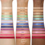 Arm swatches show ColourPop Beach Dreamin' shadow palette: 12 eyeshadows - nudes, gold shimmer, mint/teal, lilac, blues, pinks, and red - in matte and metallic finishes across three skin tones, studio close-up with shade names labeled.