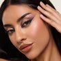 Metallic smoky eye look created with the ColourPop Shadow Palette, Precious Metals, blending shimmery rose, pewter, gold, and deep charcoal shades in a dramatic wing, shown in a close-up model face with hand at temple under soft studio lighting.