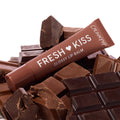 ColourPop Fresh Kiss Glossy Balm in Chocolate Milkshake lies angled atop stacked milk and dark chocolate bars, a brown squeeze tube with white lettering spotlighting the dessert-inspired glossy lip balm shade.