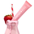ColourPop Fresh Kiss Glossy Lip Balm tube in Strawberry Milk shade resting in a dripping pink milk bottle with a red-and-white straw and a ripe strawberry on the rim, highlighting the Fruit Basket ColourPop Glossy Lip Balm Trio.