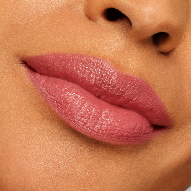 Full lips wearing ColourPop Lippie Stix “It’s Giving,” a rosy mauve pink with a creamy satin sheen, showcasing smooth, even coverage in a close-up swatch against skin for true-to-color shade reference.