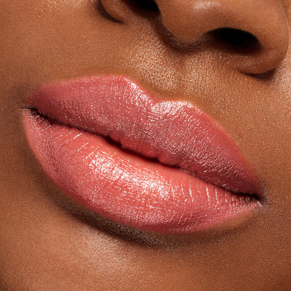 Glossy pink-coral lips wearing ColourPop Lippie Stix It’s Giving, showing a creamy, high-shine finish with smooth coverage in a tight close-up of the mouth and nose to highlight the lip color payoff and texture.