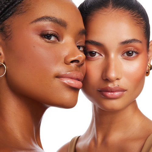 Two models showcase Shell Beach ColourPop Bronzer Stix, wearing a warm, sun-kissed bronze glow on cheeks and temples with a dewy finish, captured in a close-up studio portrait against a white background.