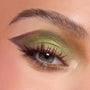 Close-up eye wearing the ColourPop Beware Ogre shadow palette, with shimmering lime and olive greens blended into a deep plum cut-crease wing, soft inner-corner glow, and defined lashes, shown on skin to highlight pigment and finish.