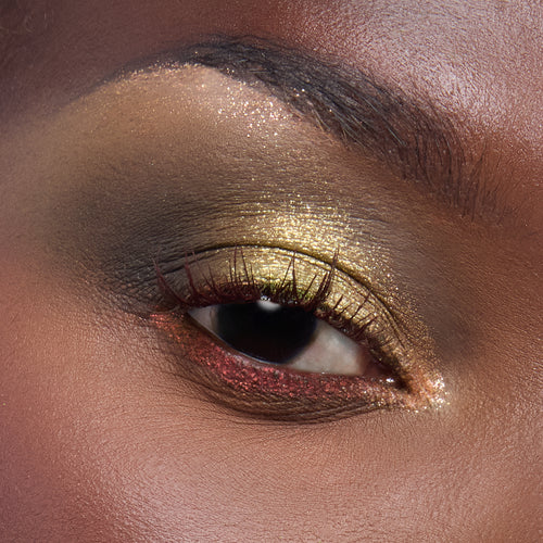 Shimmering olive-gold eyeshadow with red glitter lower liner accenting a model’s eye, showcasing the ColourPop X DreamWorks Shrek full collection set by ColourPop in a studio close-up, with smoky brown crease and sparkly inner corner.