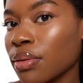 ColourPop Super Shock Highlighter in Ohana catching light on the cheekbone, delivering a luminous champagne glow on dewy skin with natural lashes and glossy lips in a close-up beauty shot.