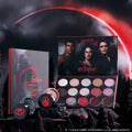 ColourPop Eternal Eclipse eye trio from the Twilight collection displayed in a dark forest scene, featuring an open eyeshadow palette with red and smokey shimmer shades and two loose shadows against a dramatic blood-red eclipse sky.