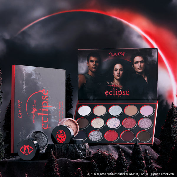 ColourPop Eternal Eclipse eye trio from the Twilight collection displayed in a dark forest scene, featuring an open eyeshadow palette with red and smokey shimmer shades and two loose shadows against a dramatic blood-red eclipse sky.