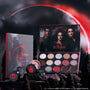 ColourPop Eternal Eclipse eye trio from the Twilight collection displayed in a dark forest scene, featuring an open eyeshadow palette with red and smokey shimmer shades and two loose shadows against a dramatic blood-red eclipse sky.