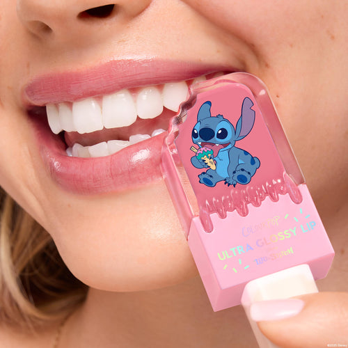 ColourPop Ultra Glossy Lip Keepin’ It Sweet coats smiling lips in a sheer pink shine as the pink tube with Disney’s Stitch graphic is held to the mouth, highlighting the high-gloss finish in a tight beauty close-up.