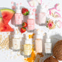 Strawberry Face Milk bottle standing center, labeled Fourth Ray Beauty, surrounded by fresh strawberries, rose petals, and assorted flavors on a white backdrop - ColourPop Face Milk, hydrating strawberry formula for glowing, dewy skin.