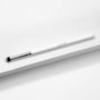 ColourPop Pencil Brush resting diagonally on a white textured block, a makeup brush with a slim white handle and logo, silver ferrule, and small tapered black-and-white bristles for precise eyeshadow and eyeliner smudging.
