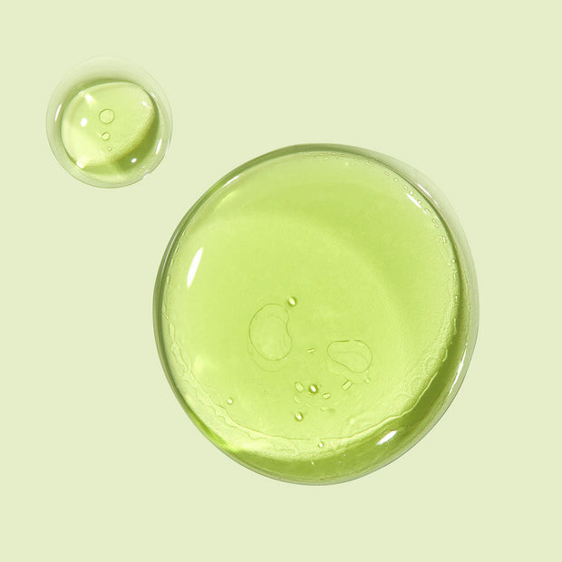Avocado + Aloe Double Shot face serum forming glossy, translucent green drops that pool on a pale mint background, highlighting a lightweight, hydrating texture; ColourPop Face Serum.