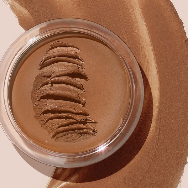 Open glass jar of ColourPop SOL Face & Body Bronzing Balm in Dark, its creamy bronzer surface swiped into ridges, set on a backdrop of blended warm-brown pigment.