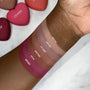 Let’s Dance shade of ColourPop Pressed Powder Blush swatched on an arm, a soft mauve-pink stripe centered among labeled hues from nude to berry, with matte heart-shaped ColourPop compacts blurred in the background.