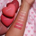 Let’s Dance ColourPop Pressed Powder Blush swatched on a forearm, second from top, alongside Kiss N Tell, Flirt Alert, 4ever Yours, Text Me, and Babycakes, with heart-shaped ColourPop compacts on pink heart-print fabric.