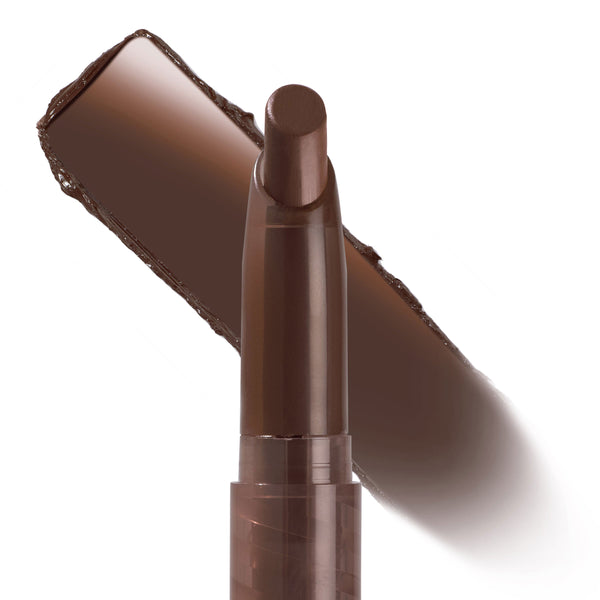 ColourPop Lippie Stix In the Nude standing upright with the bullet exposed, showcasing a deep brown nude lip color; a bold swatch streaked diagonally behind on a white background for shade reference.
