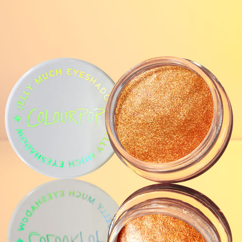 ColourPop Jelly Much Shadow in Brentwood sits open, showcasing a metallic copper-gold jelly eyeshadow with microglitter; white lid with neon green logo beside it, reflected on a glossy surface against a warm peach backdrop.