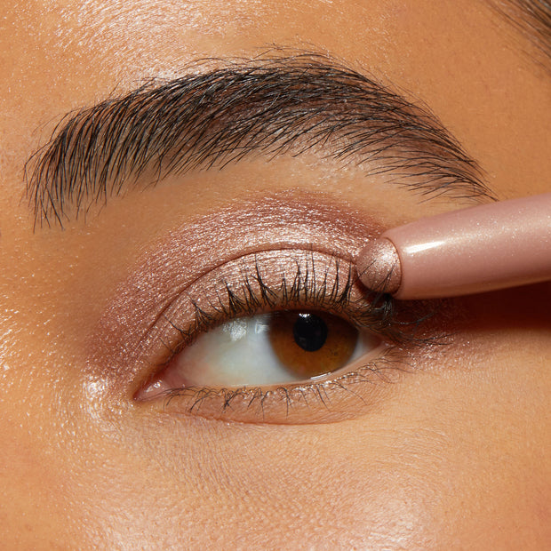 ColourPop Shadow Stix Socialite glides over the eyelid, applying shimmery rose‑champagne cream shadow in a tight close-up, showcasing metallic payoff and precise, easy application with the twist-up stick.